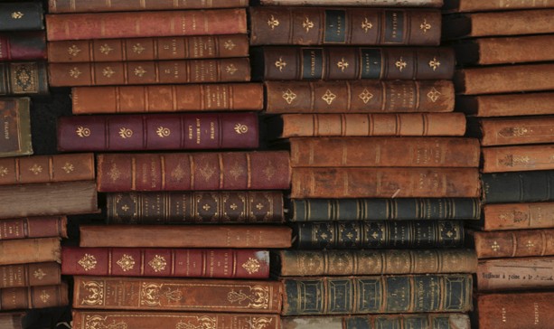 A close up of old books stacked horizontally on a shelf.