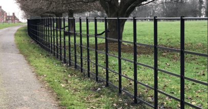 A low-level fence formed of metal bars. The vertical uprights are spaced approximately 1m apart, with 5No. round bars, approximately 300mm in diameter, forming the rails of fence. 