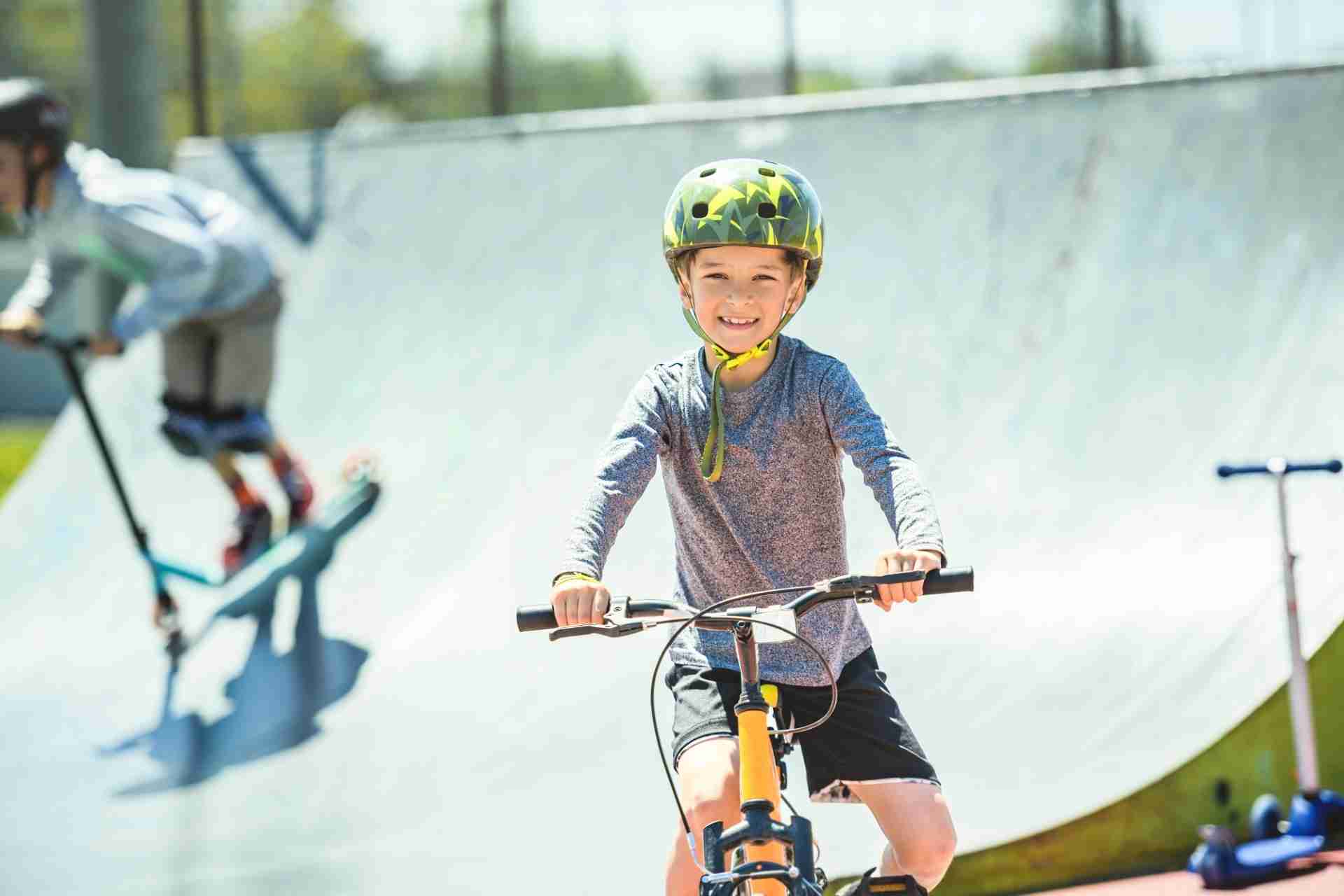 Child practicing biking at a skate park with scooters nearby.