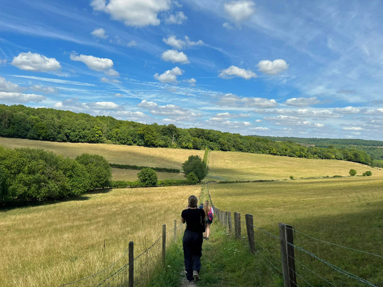 People walking down a grassy path through open fields on a sunny day.
